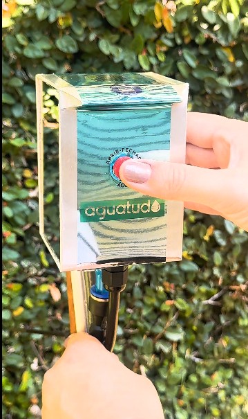 Mão pressionando o botão único do Aguatudo instalado no jardim